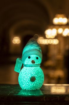 Little snowman wearing a rainbow scarf and hat against a golden light bokeh waiting for Christmas time and gifts