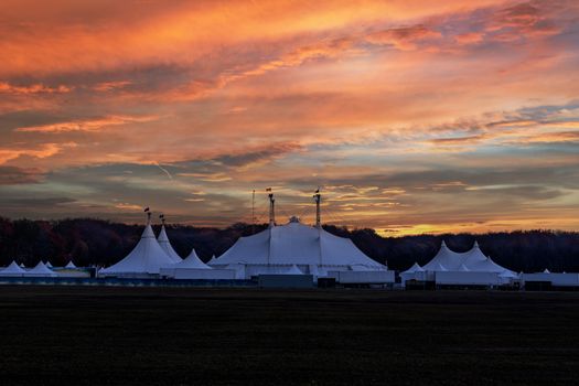 Circus tent under a warn sunset and chaotic sky without the name of the circus company which is cloned out and replaced by the metallic structure