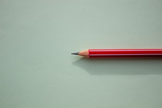 One red pencil on a light green background