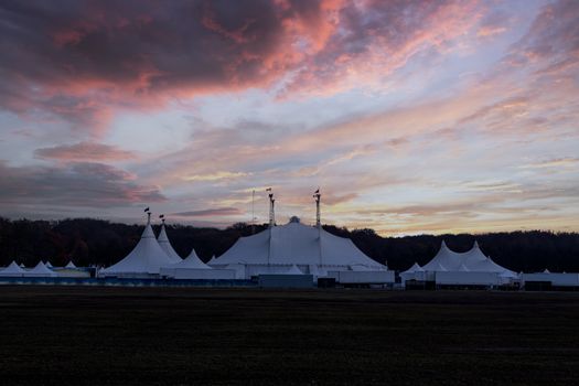 Circus tent under a warn sunset and chaotic sky without the name of the circus company which is cloned out and replaced by the metallic structure