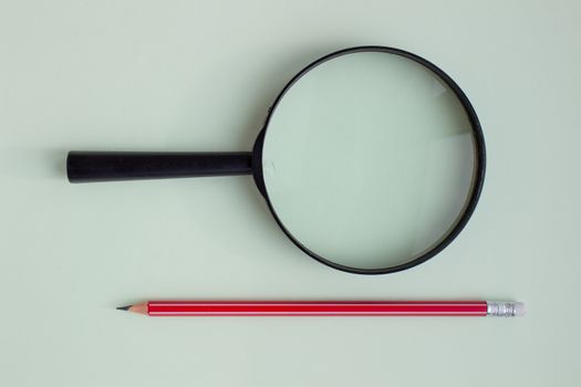 One red pencil under a magnifying glass close-up on a light background