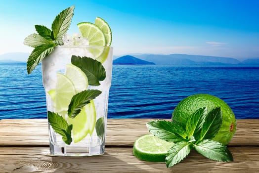 Mojito (alcoholic cocktail with rum, lime and mint) on wooden table against seascape. Clipping paths, infinite depth of field