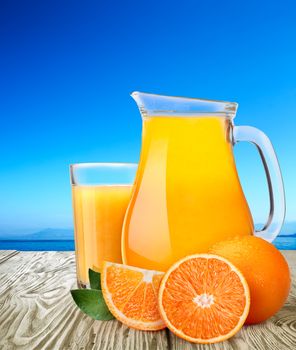 Jug or pitcher of orange juice with oranges on wooden table. Clipping path