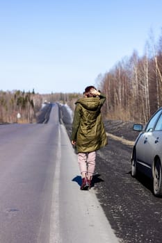 A young woman walks by the side of the road. Road in the forest.