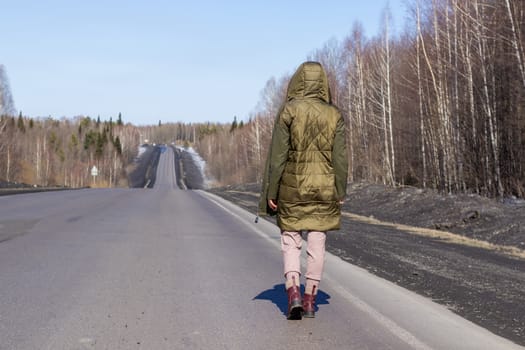 A young woman walks by the side of the road. Road in the forest.