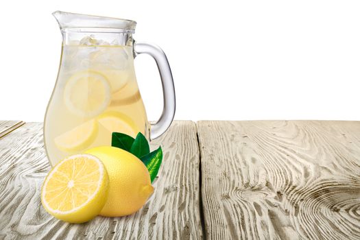 Jug or pitcher of lemonade with lemons on foreground standing on wooden table. Clipping paths for both background and pitcher, infinite depth of field