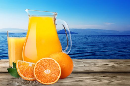 Jug or pitcher of orange juice with oranges on wooden table against seascape. Clipping paths, infinite depth of field