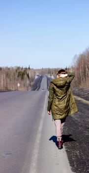 A young woman walks by the side of the road. Road in the forest.