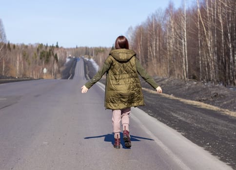 A young woman walks by the side of the road. Road in the forest.