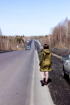 A young woman walks by the side of the road. Road in the forest.