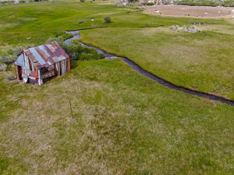 Aerial view of abandoned little small wooden house barn next small river in the green valley of a mountain, Aspen Spring, Mono County, California, USA. 