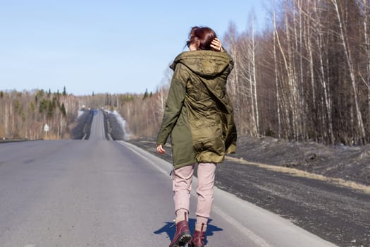 A young woman walks by the side of the road. Road in the forest.