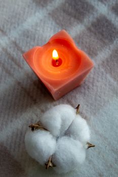 decoration, hygge and cosiness concept - burning wite fragrance candle and cotton flower on knitted blanket