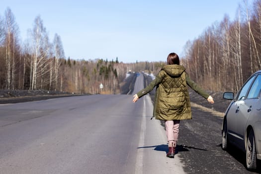 A young woman walks by the side of the road. Road in the forest.