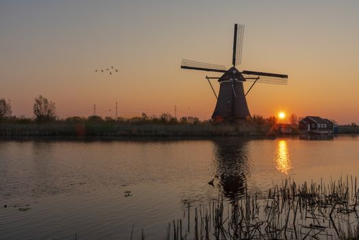 Sunrise on the alignment of windmills reflected on the calm water in the long canal 