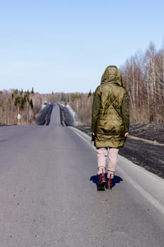 A young woman walks by the side of the road. Road in the forest.