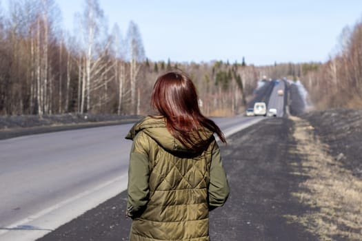 A young woman walks by the side of the road. Road in the forest.