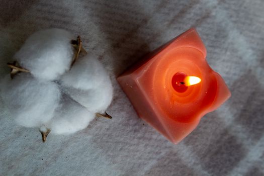 decoration, hygge and cosiness concept - burning wite fragrance candle and cotton flower on knitted blanket