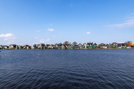 Dutch village with small red roof topped green house along of the calm canal water reflection on the water at spring time, Zaanse Schans, Netherlands
