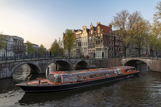 Cruse boat navigating on the narrows canals of Amsterdam under the sunset light, Amsterdam, Netherlands
