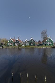 Plane flying above the Dutch green rural houses at the edge of the canals in the clear blue sunny sky