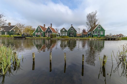 View of a reflection of the wooden green houses topped with dark orange color roof reflected on the calm water of the canal from the opposite side of the canal
