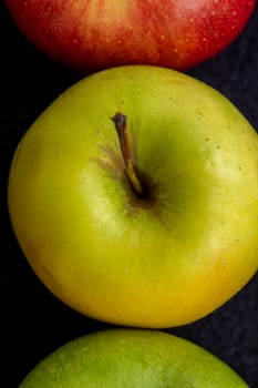 Three apples, one green and two red and yellow on a dark background.