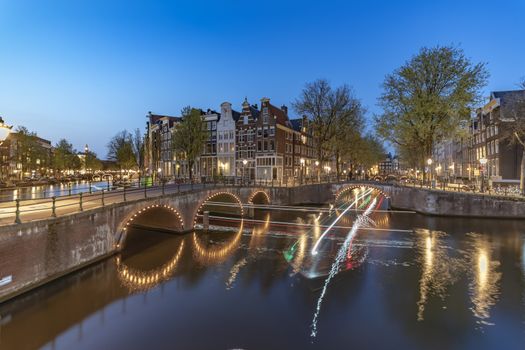 Long exposure boat cruising along the Amsterdam calm canal at the blue sunset hour, Netherlands