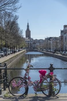 Pink and decorated bicycle lays on the bridge over a calm canal against a lamp post reflected on the water with the ST James church in the background, The Hague, Netherlands