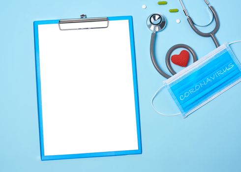 medical equipment mockup clipboard, stethoscope with red heart and drug, surgical mask on blue copy space background.