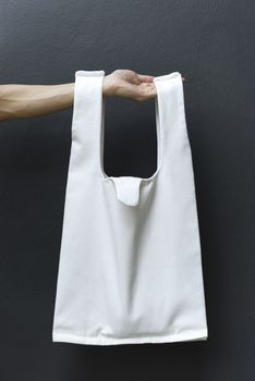 Hand Holding bag canvas fabric for mockup blank template on black wall background.