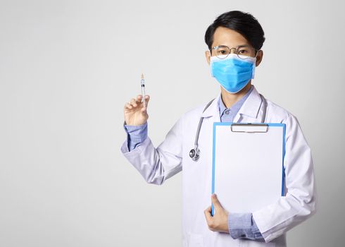 asia man doctor wearing surgical mask and hand holding vaccine syringe and paper form standing in gray wall background. Concept Preventive measures against corona virus.