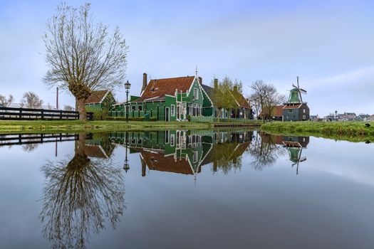 ZAANSE SCHANS, 14 April 2019 - Reflection of the wooden green houses topped with dark orange color roof reflected on the calm water of the canal