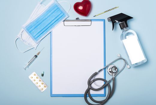 medical equipment mockup clipboard, stethoscope with red heart and drug, surgical mask on blue copy space background.