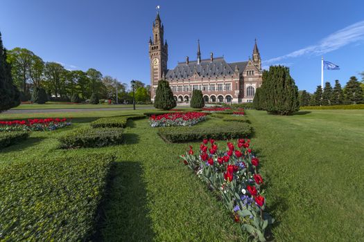 THE HAGUE, 24 April 2019 - Sunrise at the Peace Palace, seat of the International Court of Justice, view from the peaceful garden with read tulip flowers around the building 