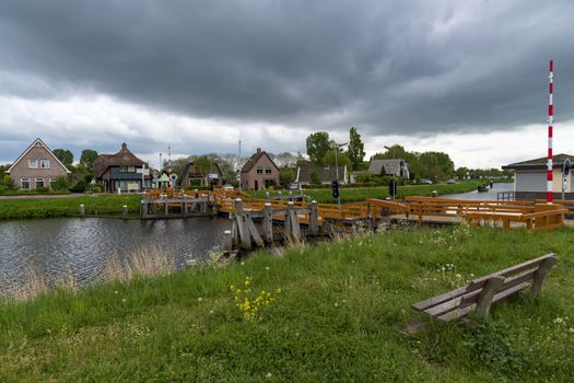 Empty wooden bench facing the mobile bridge over the canal under a straightening heavy dark cloud and coming storm 