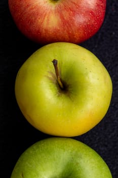 Three apples, one green and two red and yellow on a dark background.