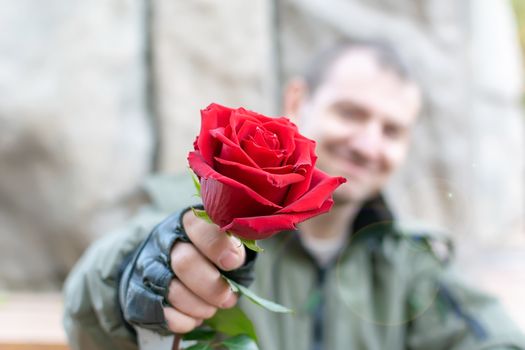 hand of a man in leather gloves and handcuffs gives a red rose flower