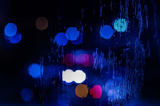red and blue night police lights bokeh trough wet glass close-up with selective focus abstract background