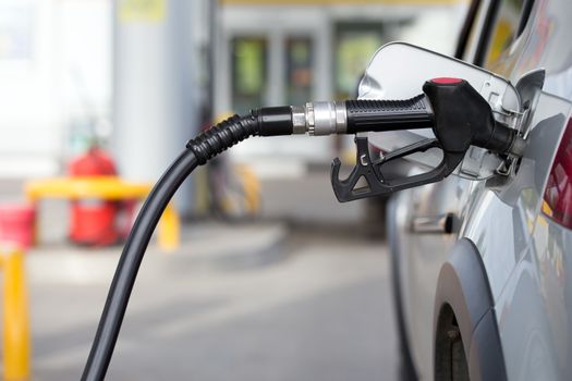 silver car refueling on night gas station - close-up with selective focus and blurry background.