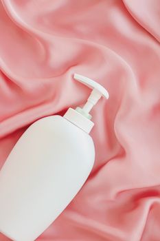 Blank label cosmetic container bottle as product mockup on pink silk background, hygiene and healthcare