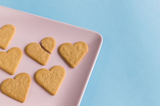 Broken heart. Broken cookie in the middle of the complete ones on a pink tray and light blue background. Copy space. Top view.