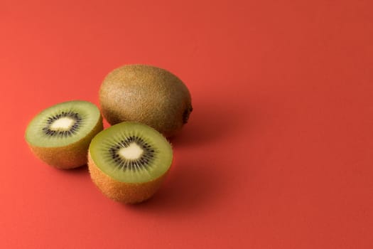 Close-up of two kiwis, one of them cut in half. Isolated on a red background. Copy space.