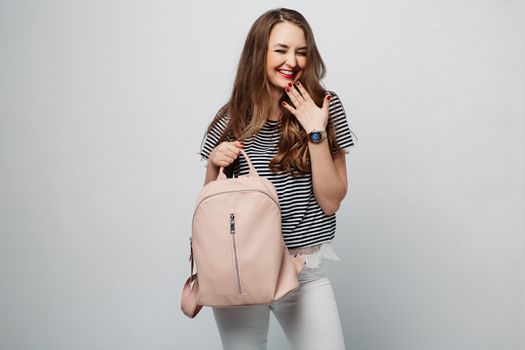 Beautiful and sexy brunette woman after beauty salon, sensuality posing, touching wavy hair by hand and smiling. Fashionable girl in striped blouse and white jeans posing holding beige leather bag.