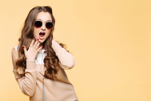 Studio portrait of beautiful shocked emotionally woman surprising looking at camera with opened mouth, touching face by hands and screaming. Stylish girl in beige dress, wavy hair, perfect manicure.