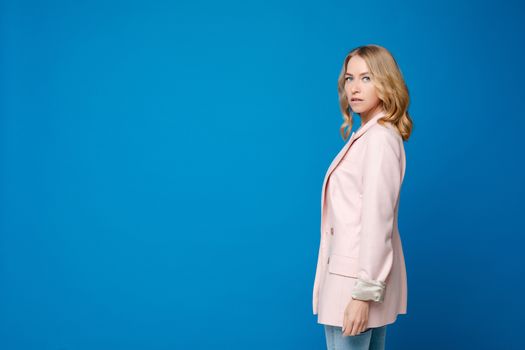 Beautiful caucasian woman with light wavy hair in a white shirt and blue trousers isolated on blue background