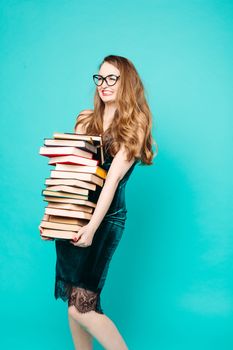 Portrait of emotionally shocked sexy teacher in dress with lace, eyeglasses, holding many books and surprised looking at camera. Young teacher or student screaming. Blue studio background.