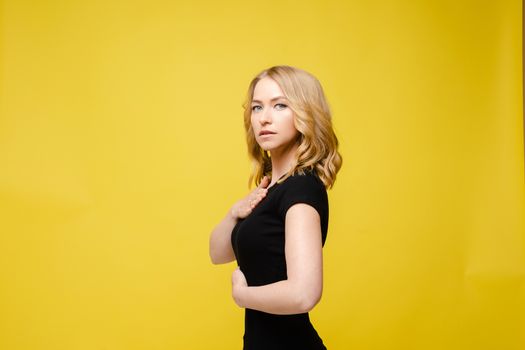 Beautiful caucasian woman with light wavy hair in a black t-shirt isolated on yellow background