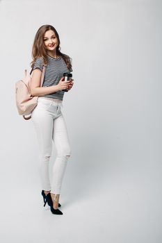 Pretty and stylish brunette girl with red lips, long wavy hair after beauty salon and shopping, posing at studio, holding thermos with warm coffee or tea. Sensuality fashionable woman looking down.