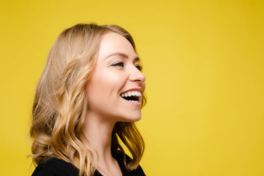 Beautiful caucasian woman with light wavy hair in a black t-shirt laughs isolated on yellow background